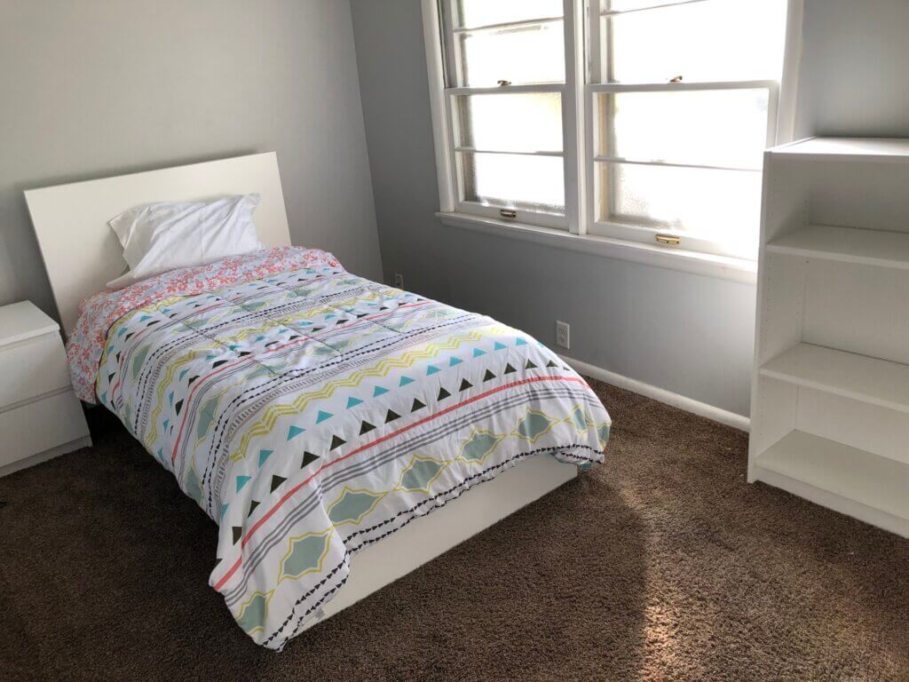 Youth bedroom with twin bed that is covered with a white bedspread that has colored patterns