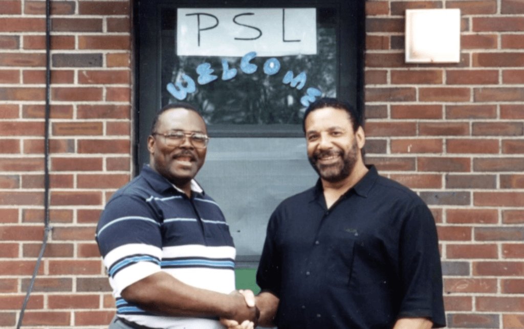 Oscar Reed and Jim Marshall shaking hands under sign that reads PSL