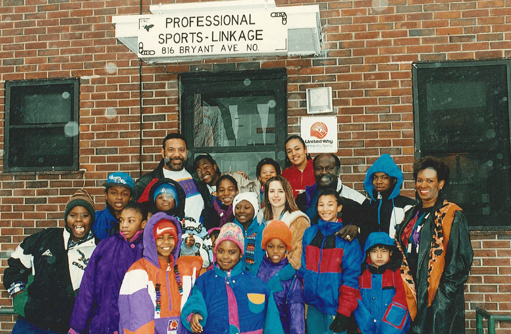 Founders Jim Marshall and Oscar Reed standing with group of youth outside building with sign that reads "Professional Sports Linkage"