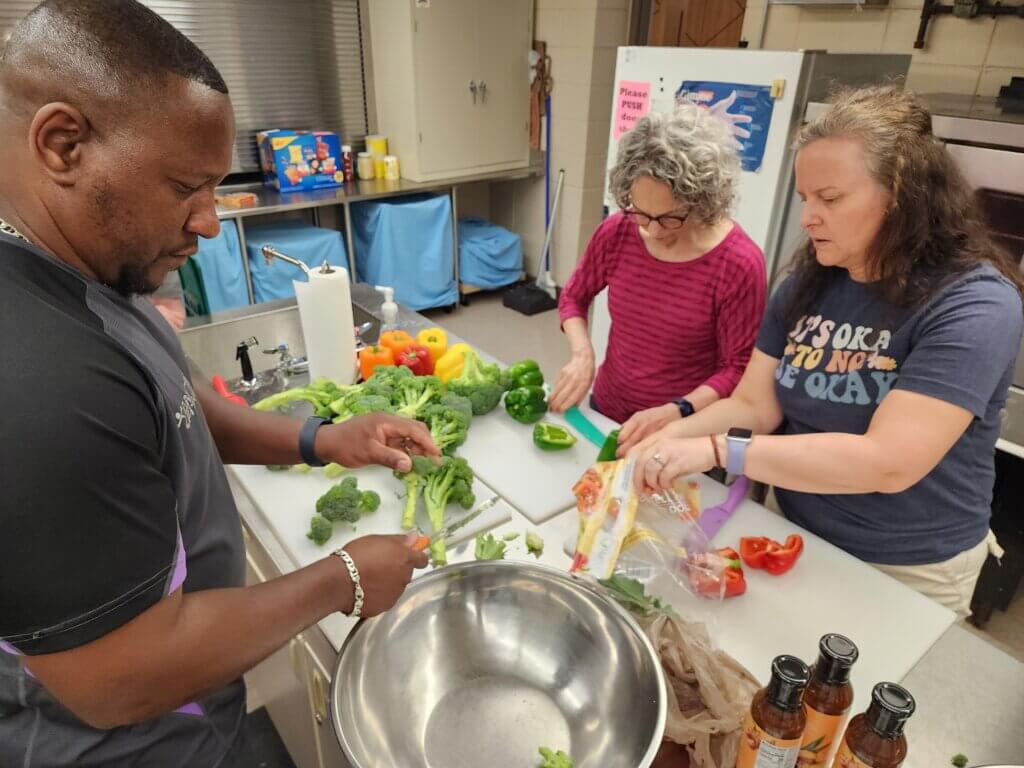 Three volunteers cutting vegetables to make meals.