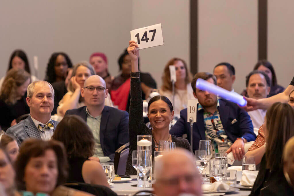 Woman seated in crowd holding bid card in air