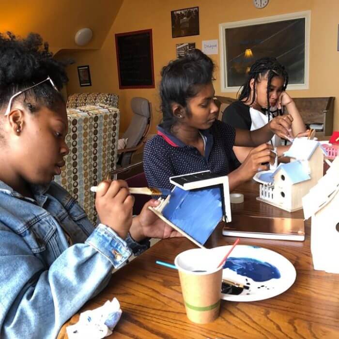 Three female youth painting birdhouses