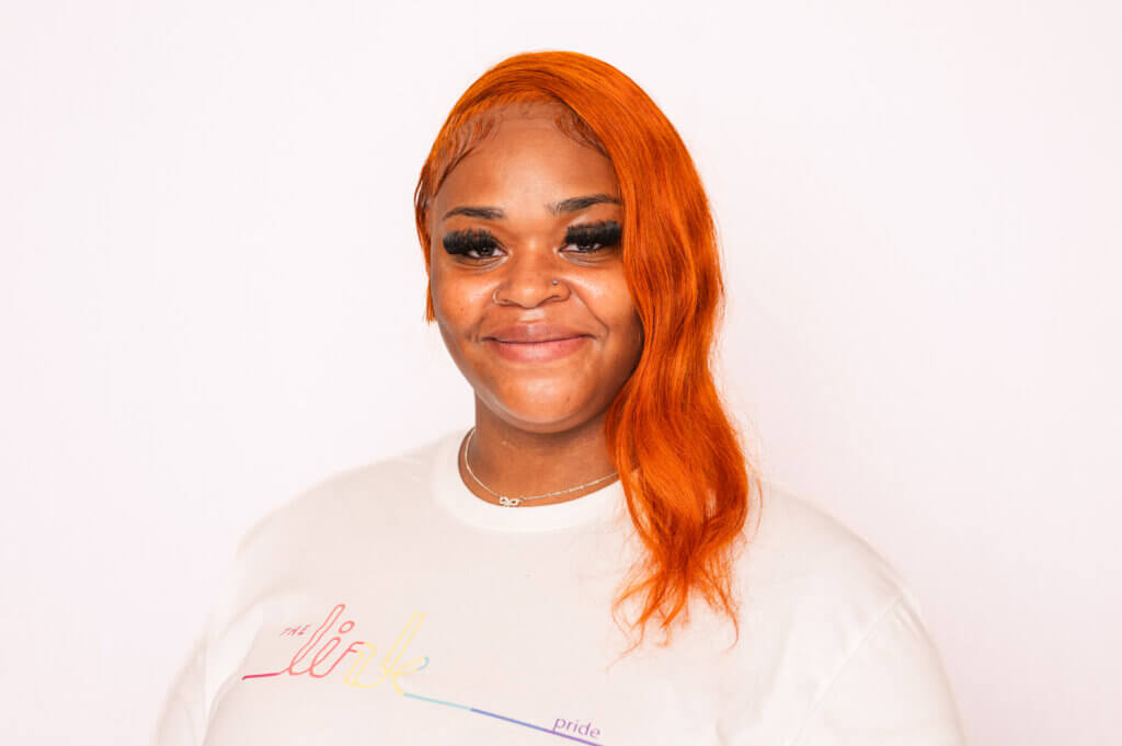 Youth with orange hair wearing white Pride t-shirt in front of white background